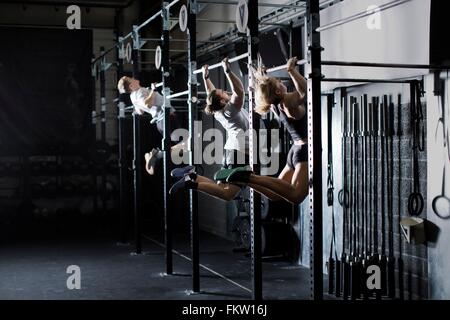 Three young adults training on wall bar in gym Stock Photo