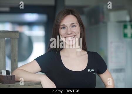 Portrait of young female waitress in cafe leaning against shelf Stock Photo