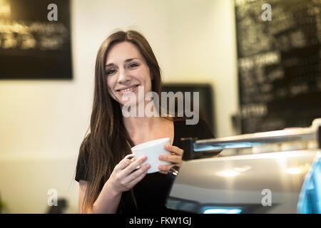 Portrait of young female waitress holding coffee cup in cafe Stock Photo