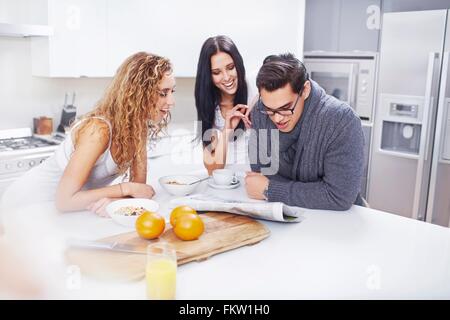 Three young adults reading newspaper at kitchen counter Stock Photo