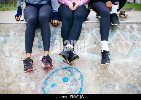 Waist down view of three young women skateboarders sitting in skateboard park Stock Photo