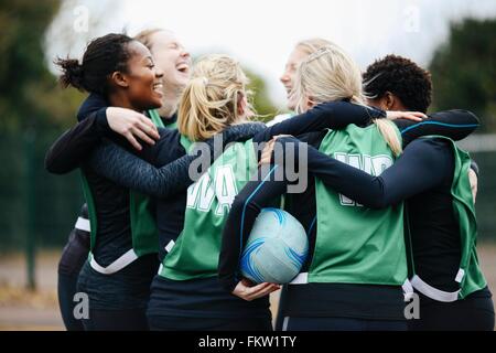 Female netball team celebrating in huddle on netball court Stock Photo