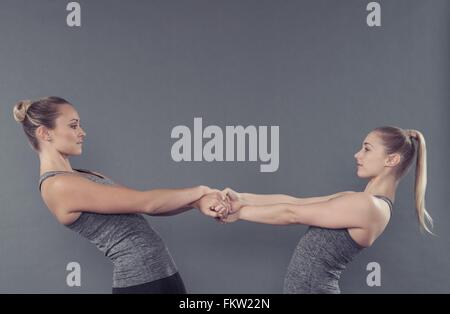Young women stretching, holding hands, grey background Stock Photo