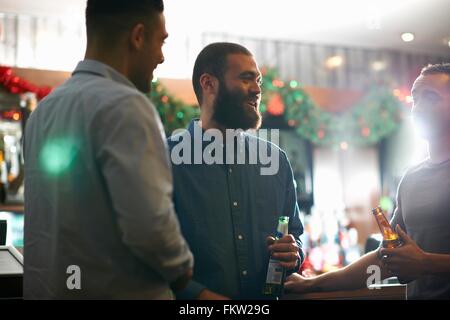 Young men in public house holding beer bottles leaning against counter smiling Stock Photo