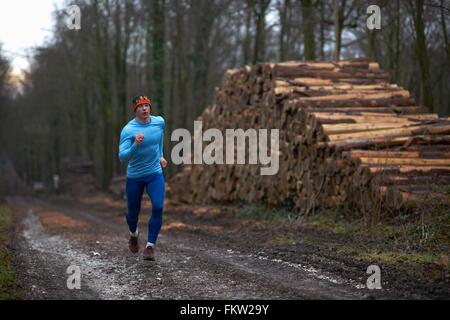 Full length view of runner running on treelined path by stack of logs Stock Photo