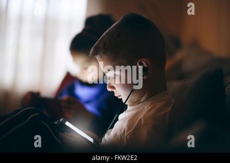 Side view of boy on sofa wearing earphones looking down using digital tablet Stock Photo