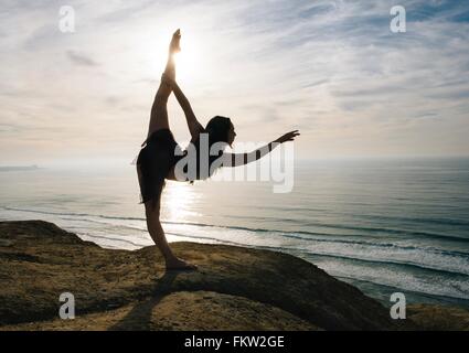 Young female dancer standing on rock, holding leg, stretching in elegant pose, San Diego, California, USA Stock Photo