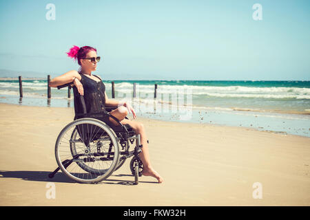 Disabled woman in the wheelchair at the beach. Cross-processed and color-toned image. Stock Photo