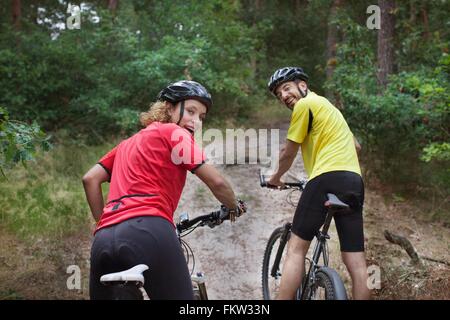 Portrait   mountain biking couple looking over their shoulders in forest Stock Photo