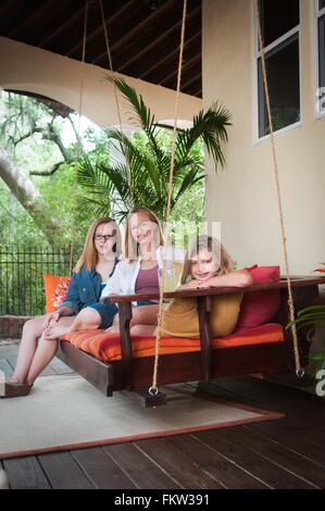 Mother with daughters, sitting on porch swing looking at camera smiling Stock Photo