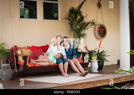 Mother with daughters, sitting on porch swing looking at camera smiling Stock Photo