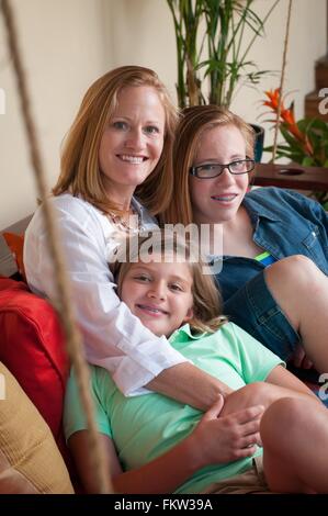 Mother sitting with daughters looking at camera smiling Stock Photo