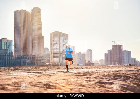 Mid adult man running on sand by skyscrapers, Dubai, United Arab Emirates Stock Photo