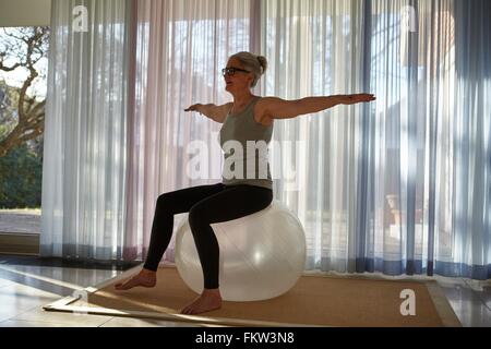 Mature woman balancing on exercise ball in front of patio doors Stock Photo