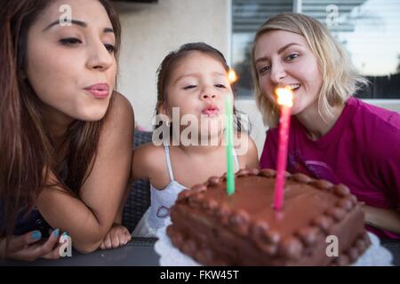 Young girl sitting with family, blowing out candles on birthday cake Stock Photo