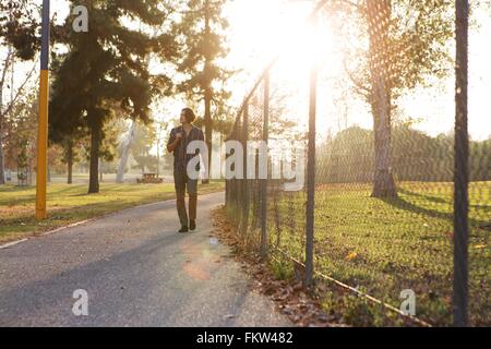 Full length front view of young man walking on pathway  through park looking away Stock Photo