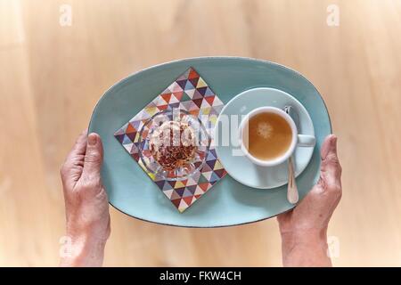 Overhead view of female hands holding plate of dessert and cup of espresso Stock Photo