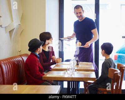 Waiter serving lunch in restaurant to woman and sons Stock Photo