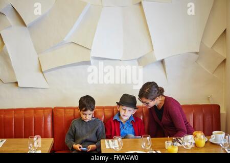 Mother and sons using digital tablet and smartphone in restaurant Stock Photo
