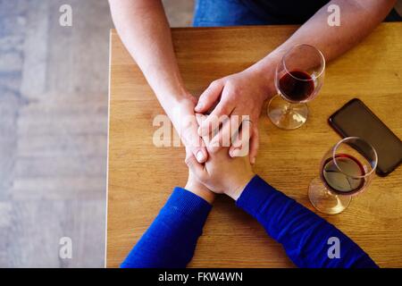 Overhead cropped view of romantic couple holding hands in restaurant Stock Photo