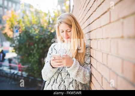 Woman texting on smartphone, against brick wall Stock Photo