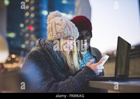 Couple using smartphone and laptop outdoors at dusk Stock Photo
