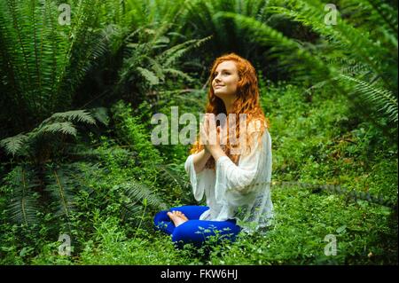 Young woman in forest practicing yoga in lotus position Stock Photo