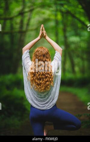 Rear view of young woman in forest practicing yoga in tree pose Stock Photo