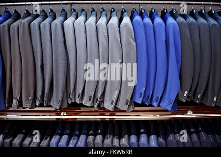 Elegant blue and gray suits on hangers are seen in a suit store Stock Photo