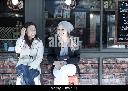 Two women friends sitting outside city cafe Stock Photo