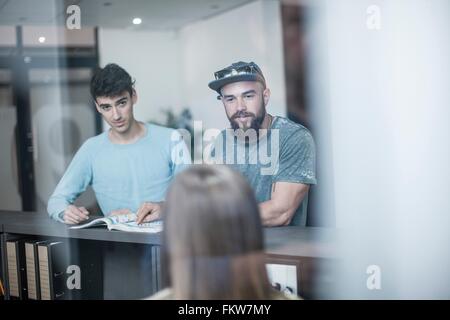 Two young men querying receptionist in office Stock Photo