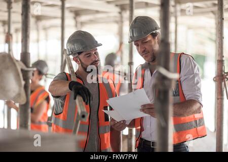 Male builders looking at blueprint on construction site Stock Photo