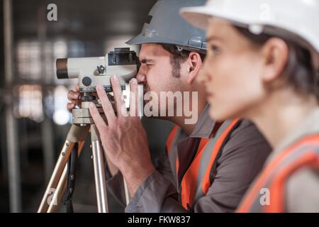 Female and male surveyors looking through theodolite  on construction site Stock Photo
