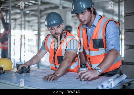 Site foreman and builder looking at blueprint in construction site Stock Photo