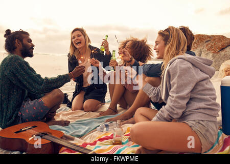 Happy friends partying on the beach with drinks and sparklers. Diverse group of friends together at the beach celebrating new ye