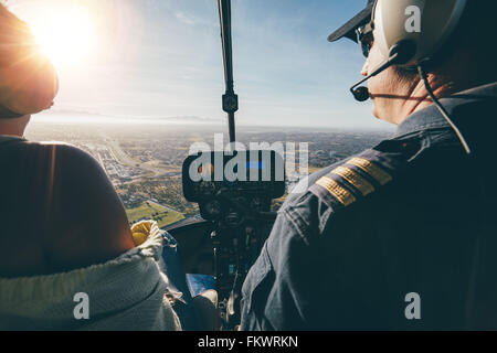 Rear view of two pilots flying a helicopter on sunny day. Close up shot of pilots sitting in the cockpit with bright sunlight. Stock Photo