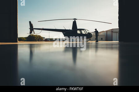 Silhouette of helicopter in the hangar with a pilot. Pilot doing preflight inspection of a helicopter. Stock Photo