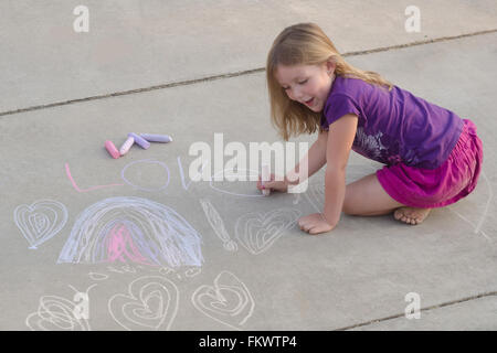 A six year old girl creates her designs on a sidewalk with chalk Stock Photo