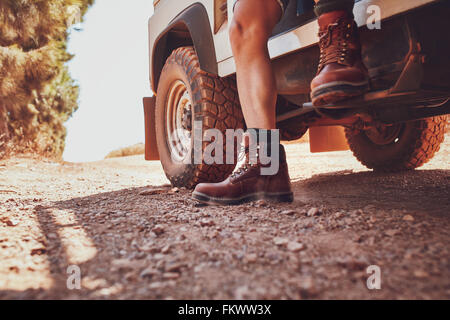 Close up of male leg with leather boot stepping out of a off road vehicle. Car parked on the dirt road in countryside. Stock Photo