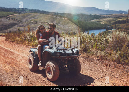 Young couple having fun on mountain while driving a quad bike on a summer day. Young man and woman on an ATV. Stock Photo
