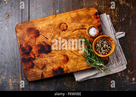 Chopping cutting kitchen board, salt, pepper and rosemary on dark wooden background Stock Photo