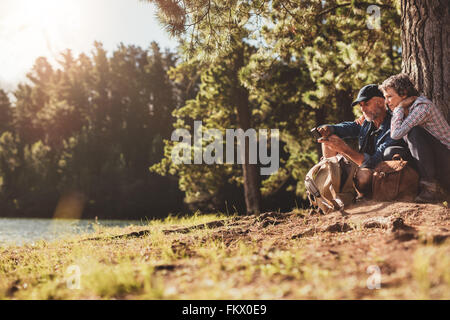 Portrait of senior couple sitting by a lake on a summer day. Mature man and woman using compass for directions. Stock Photo