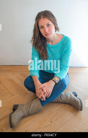 Young woman sitting on the floor, crossing legs. Stock Photo
