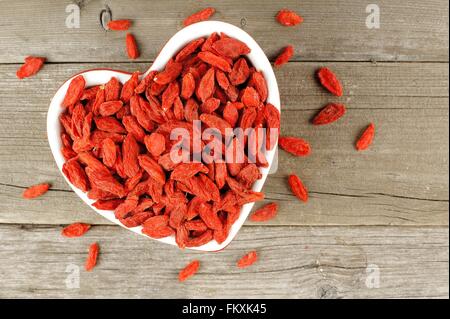 Heart shaped bowl filled with dried goji berries over a wood background Stock Photo