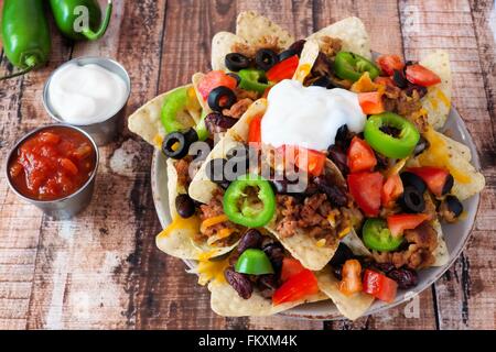 Plate of Mexican nacho chips topped with sour cream, ground meat, jalapenos, tomatoes, beans and melted cheese Stock Photo