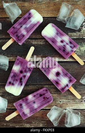 Group of homemade blueberry vanilla popsicles with ice cubes on a rustic wood background