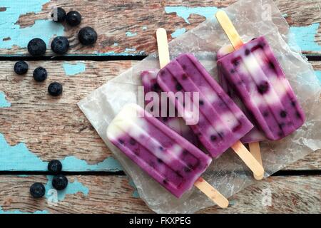 Homemade blueberry vanilla ice pops in a cluster on paper with rustic wood background Stock Photo