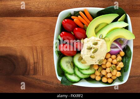 Nutritious lunch bowl with avocado, hummus and mixed vegetables, overhead view in square bowl on wood Stock Photo