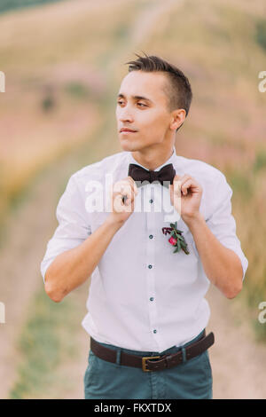 Handsome groom adjusts bowtie. Alpian meadow on background Stock Photo
