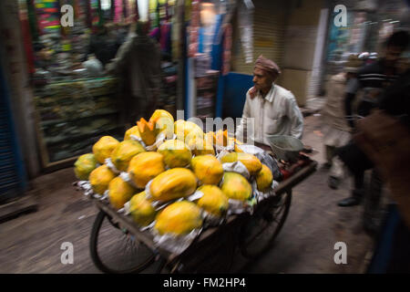 Asia, India, New Delhi, fruit stand vendor pushes cart full of papayas down the crowed streets. Stock Photo